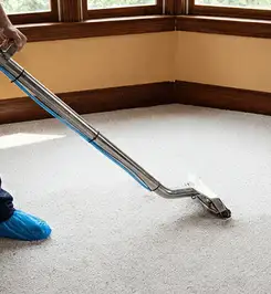 Steam carpet cleaning technician using a hot-water extraction wand on a residential carpet, wearing blue protective shoe covers Orlando, FL.