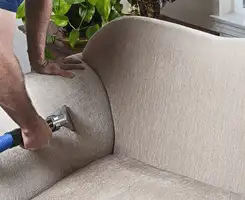 Professional upholstery cleaner deep-cleaning a fabric sofa with a handheld extraction tool and hose in Orlando, FL.